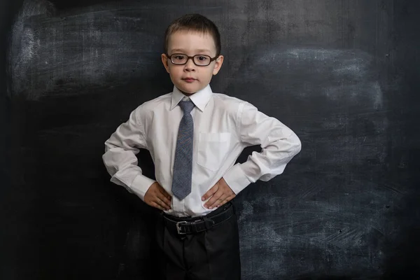 Jonge kinderen staande in de buurt van een schoolbord met zijn handen in de zijkanten, bazig pose. Terug naar school-concept. Slim en slimme preschool jongen. — Stockfoto