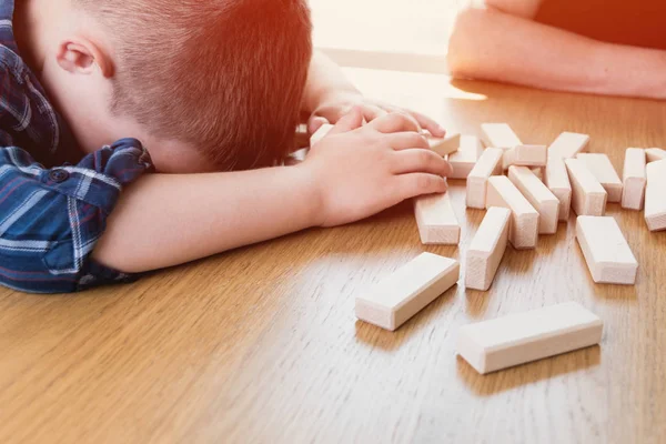 Kid lost the jenga game. His tower from wooden blocks had fallen. Concept of risk and strategy in business and construction.