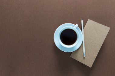 Üstten görünüm defter, fincan kahve ve kalem ile çalışma masası üzerinde. Metin için yer kopyalayın. Kahverengi zemin üzerine bir çalışma alanı'nın düz yatıyordu.
