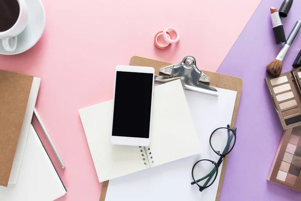 Görünümü ile açılan dizüstü bilgisayarlar, kahve güzellik çalışma masası üzerinde top, kalem, fırça, ruj, göz gölgeler, kağıt, gözlük ve telefon Danışma tüm makyaj. Metin için yer kopyalayın. Düz pembe ve mor arka plan üzerinde yatıyordu.
