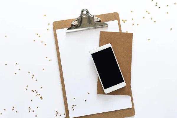 Üstten görünüm kağıt, dizüstü bilgisayar ve telefon üstünde rasgele droped altın yıldız ile çalışma masası üzerinde. Metin için yer kopyalayın. Düz beyaz arka plan üzerinde bir çalışma alanı'nın yatıyordu.