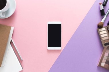 Görünümü ile dizüstü bilgisayarlar, kahve güzellik çalışma masası üzerinde en çok, kalem, makyaj fırça, ruj, göz gölgeler, kağıt, telefon Danışma her yerinde. Metin için yer kopyalayın. Düz pembe ve mor arka plan üzerinde yatıyordu.