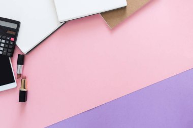 Üstten görünüm güzellik çalışma masası ile defter, hesap makinesi, kalem, ruj, Resepsiyon tüm telefon üzerinden. Metin için yer kopyalayın. Düz pembe ve mor arka plan üzerinde yatıyordu.