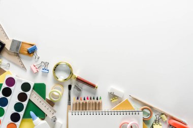 Üstten görünüm bir dizüstü, boyalar, kalemler, cetveller, ataç, iğne, hesap makinesi, muhteşem cam, tutkal, kalemtıraş ve beyaz bir arka plan üzerinde silgi. Geri okul kavramı. Ofis malzemeleri düz yatıyordu.