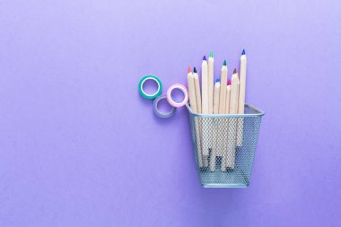 Bir kova ile renkli kalemler ve açık bir menekşe renkli kayıtlarda. Geri okul kavramı