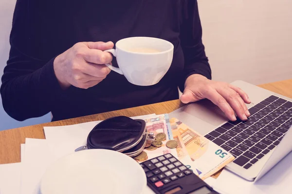 Budget planing concept. Side view of a woman drinking coffee while summing up her budget with the help of calculator and a laptop to create a plan for shopping and savings. Family budget concept. Reasonable income and expence. Copy space.