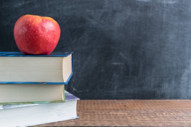 Okul malzemeleri ahşap bir masa üzerinden yan görünüm üstünde o. Üstte bir elma ile kitap yığını. Geri okul kavramı