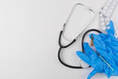 Beyaz bir arka plan üzerinde üstten görünüm bir stetoskop, farklı hapları, termometre, ampül, şırınga ve mavi eldiven. Grip ve mevsimsel hastalıklar kavramı.