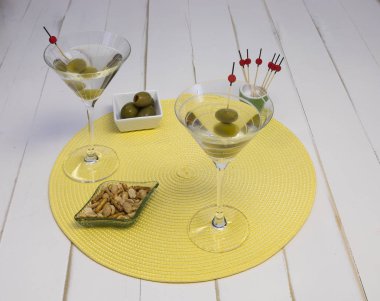 Two vodka martinis in glasses with olives and snacks on a placemat, front view. clipart