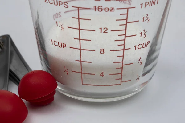 White cane sugar in a measuring cup with measuring spoons.