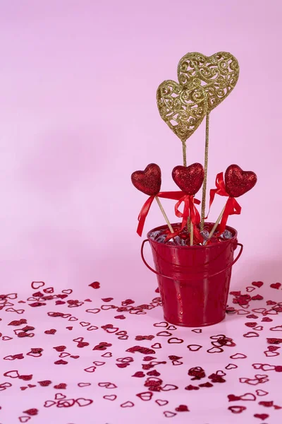 Valentine\'s Day bucket with red and gold decorative hearts on pink background.