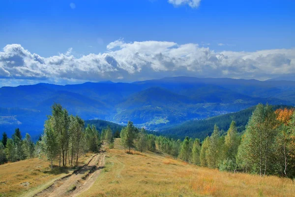 Village road among mountain meadows in autumn colors. — Stock fotografie