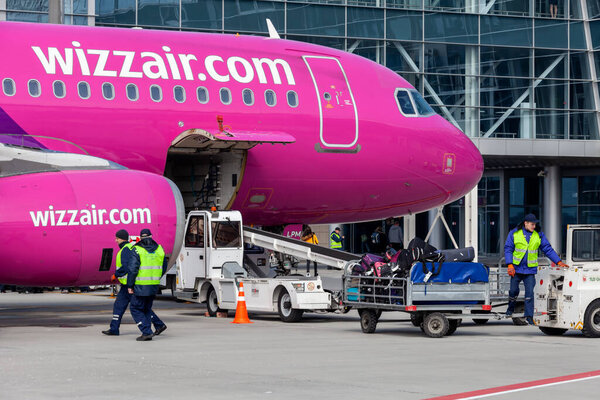 Львов, Украина - март 2018: Сотрудник аэропорта перевозит багаж на тележке в аэропорту. Наземная обработка самолетов. Львовский международный аэропорт имени Даниила Галицкого. HA-LPM, Airbus A320, Wizzair
.