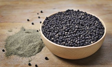 Karabiber ve öğütülmüş karabiber, düzenleme bir ahşap kase. Kara biber, madde sahne ve ahşap masa yemek atış kapatın. Üstten görünüm.