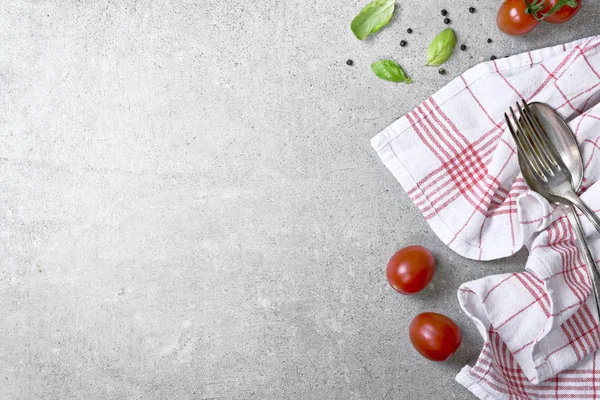 Italian cuisine or cooking background with concrete texture and fresh cooking ingredients. Tomatoes, basil, napkin and cutlery with copy space.
