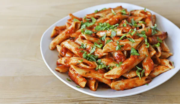 Delicious pasta dish with fresh basil on a wooden table. Top view scene, healthy eating or healthy lifestyle. Penne napoli or pasta arrabiata, closeup shot.