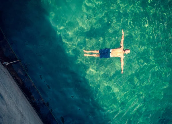 夏の休暇を楽しんでいる透明な水に浮かぶ完璧なストング体とハンサムな男 プールに浮かんでいる男の鳥瞰図 — ストック写真