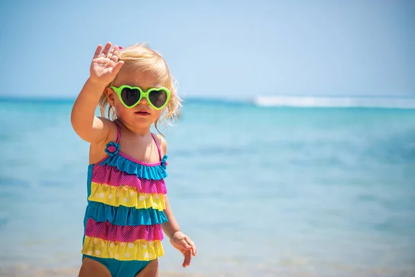 サングラス スタイリッシュなカラフルな水着 子供のファッション Seashor Smalll モデルポーズを着てビーチでかわいいブロンド女の子 — ストック写真