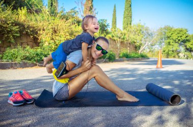 Sağlıklı aile hayatı, Erkek sevimli neşeli bebek domuzcuk geri çalış ve germe, güzel bir kadın spor excercises açık havada yapıyor küçük oğlu ile yapması için yardımcı olur