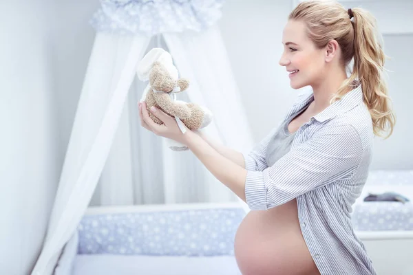 美丽的孕妇站在孩子的房间里 手里拿着软玩具 装饰和固定在卧室里的一切 为她的婴儿 照顾婴儿舒适 — 图库照片