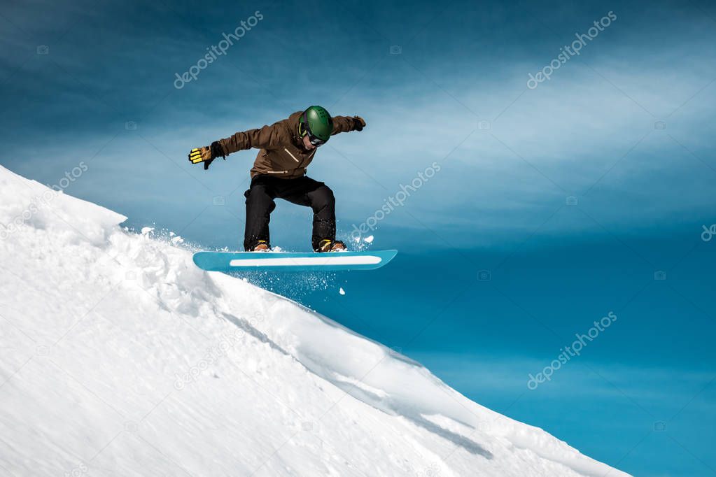 Snowboarder performs a trick on the slope in a snow-capped mountains, amazing sunny winter day, extreme wintertime holiday