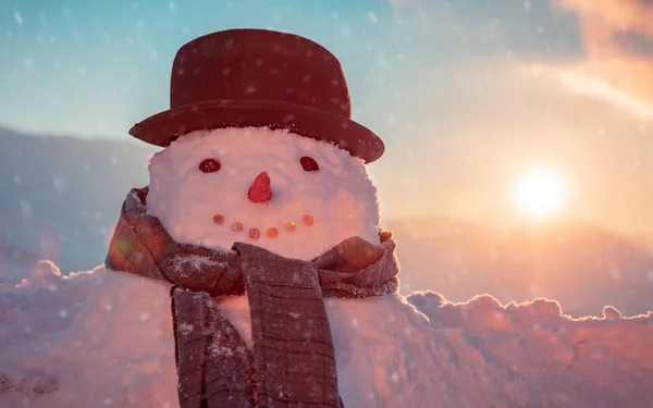 照片上是一个可爱的雪人 头戴时髦的帽子 头戴围巾 在一个白雪蒙蒙的夜晚 背景是夕阳西下 寒假快乐的传统 — 图库照片