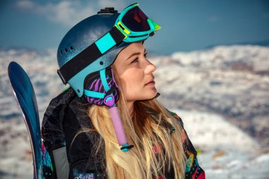 Kasklı ve maskeli bir sporcunun portresi elinde snowboard ile bir tarafa bakıyor, güneşli bir günün tadını çıkarıyor, snowboard yapmak için mükemmel bir gün.