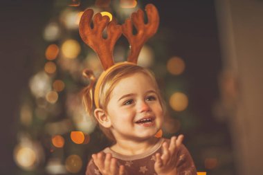 Kırmızı burunlu Rudolph kostümü giyen, Noel ağacının güzel ışıkları üzerinde çekilen, matinede eğlenen küçük bir çocuğun portresi.