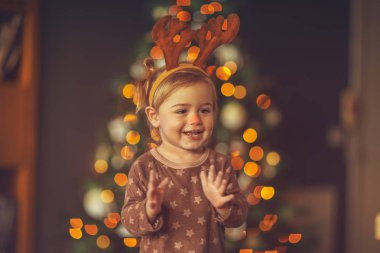 Küçük şirin bir çocuğun portresi, çocukların Noel partisinde eğleniyor, bebek çocuk Rudolph boynuzları takıyor, gülüyor ve alkışlıyor.
