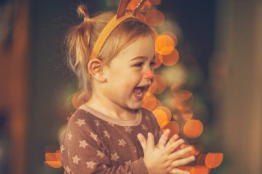 Küçük şirin bir çocuğun portresi, çocukların Noel partisinde eğleniyor, bebek çocuk Rudolph boynuzları takıyor, gülüyor ve alkışlıyor.