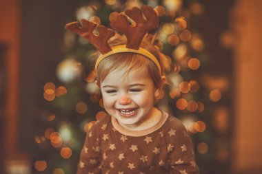 Rudolphs 'un ren geyiği kıyafeti giyen neşeli bir bebeğin portresi. Noel' i evde, parıldayan güzel bir Noel ağacının yanında geçirmek büyük bir zevk.