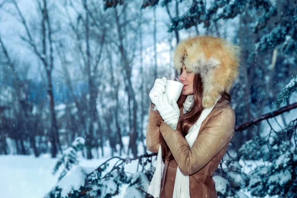 穏やかな内容の女性は喜んで雪に覆われた木の間でホットコーヒーを飲み 公園を歩く冬の休日を楽しんでいます — ストック写真