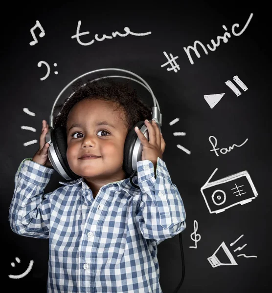 Portrait of a cute little african-american boy with pleasure listening music, happy child wearing headphones isolated over black background with different musical inscriptions — Stock Image Portrait Cute Little African American Boy Pleasure Listening Music Happy Royalty Free Stock Photos