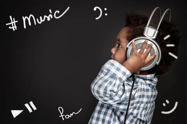Cute little african american boy wearing earphones, listening and recording baby songs, portrait over blackboard background, happy little singer — Stock Image Cute Little African American Boy Wearing Earphones Listening Recording Baby Stock Photo