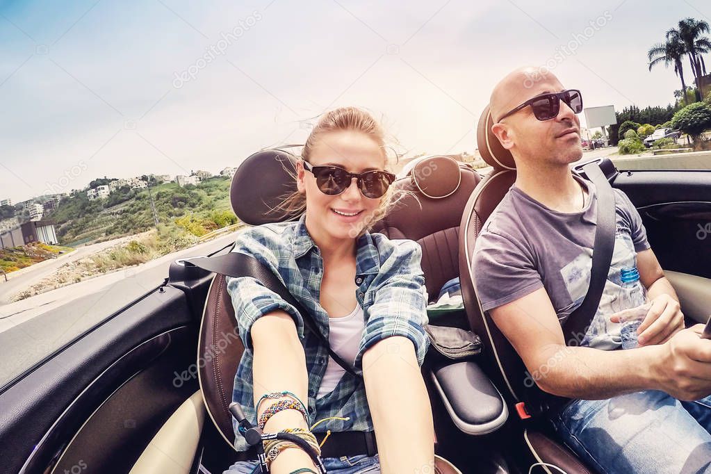 Happy couple driving open car and making selfie, honeymoon vacation in convertible auto, soul mates enjoying road trip, enjoying summer