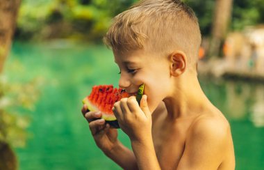 Küçük çocuk karpuz yiyor.