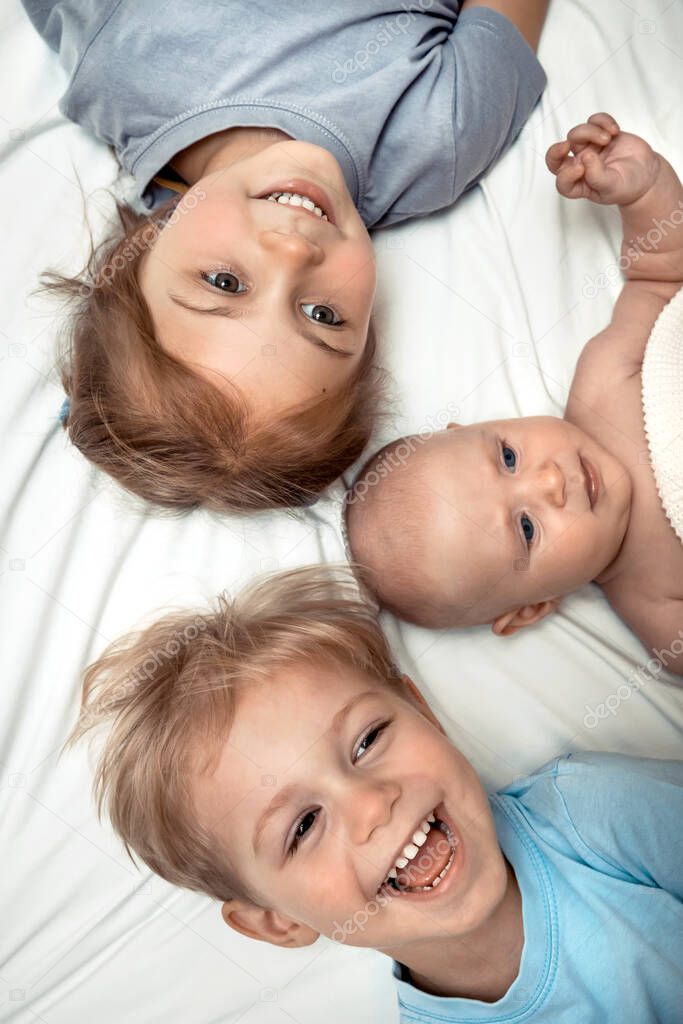 Portrait if a three cute little kids laying down on the bed at home, adorable siblings having fun together, happy family lif