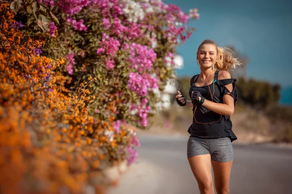 美丽绽放的花朵中的纤细女子 活跃的女性在户外跑步和听音乐 体重减轻 快乐健康的生活方式 — 图库照片