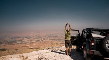 Tourist on the Break from a Long Ride. Standing near the Car and Stretching. Enjoying Amazing View of Bekaa Valley. Active Summer Vacation. Road Trip. Freedom Concept. Lebanon clipart
