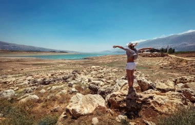 Happy Woman with Raised up Hands Standing Near Lakes and Enjoying Amazing View. Beautiful Stony Landscape in the midst of Valley. Travel Along Lebanon. clipart