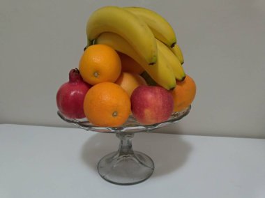 Çeşitli meyve, beyaz bir masada - elma, muz, nar, narenciye renkli plaka