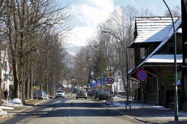 Zakopane, Polonya - 22 Mart 2018: Şehrin caddeleri üzerinde küçük trafik var. Caddenin her iki tarafında orada ağaçlar ve yol işaretleri ve uzaktan karla kaplı bir tepe görülür