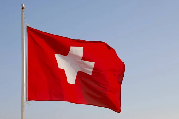 在阳光明媚的日子里 在风中飞翔的瑞士旗帜被看见在蓝天的背景下 — 图库照片