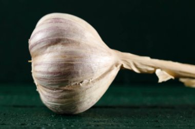 Burada koyu yeşil ahşap bir yüzeyde duran bir sarımsak var..