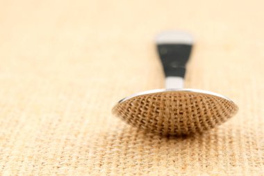 Bir kaşık keten brandanın üzerinde yatıyor. Bu tuval kaşığın parlak kısmına yansıyor..