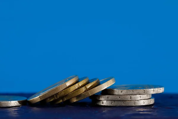 A few Euro coins on blue background. The surface on which these coins are placed is dark blue.