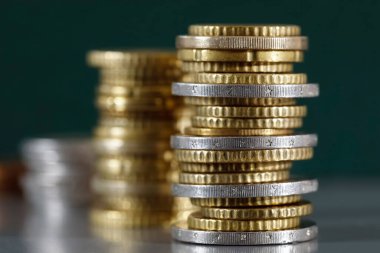 Burada gri, düz bir yüzeye ve koyu yeşil bir arkaplana karşı istiflenmiş üç bozuk para yığını var..