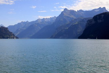 Dağlar, Lucerne Gölü 'nün eteklerinde kayalık dağların zirveleriyle uzanır. Bu manzara İsviçre 'deki Schwyz kantonundaki Brunnen' den Lucerne Gölü 'nde görülebilir..