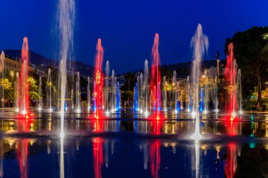 Nice, Fransa - 25 Mayıs 2018: Promenade du Paillon, yeşil bir kentsel park ile çevrili Çeşme yansıtan kırmızı ve mavi ışıkları ile Place Massena veya Massena Meydanı'nda gün batımında alev aldı.