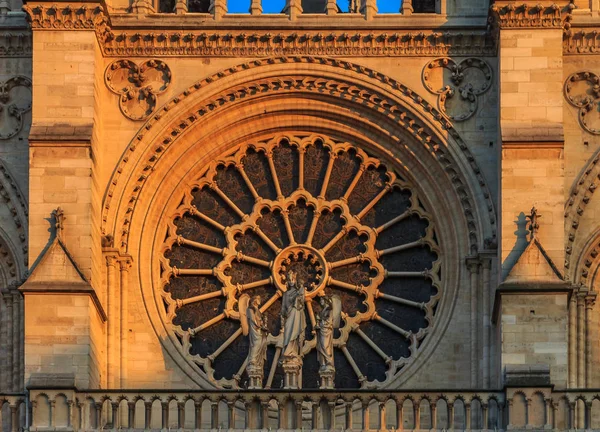 Closeup view of the Notre Dame de Paris Cathedral facade with the oldest rose window installed in 1225 which forms a halo above the Virgin with Child statue placed in front of it, colored by the warm light of sunset